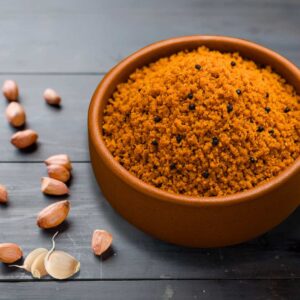 A kraft pouch labeled 'Peanut Chutney' featuring maroon, spiced peanut powder with visible texture, styled beside peanuts and chilies